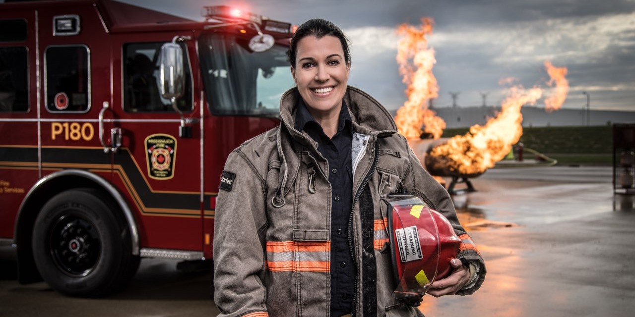 A female firefighter in standing in front of a fire truck.